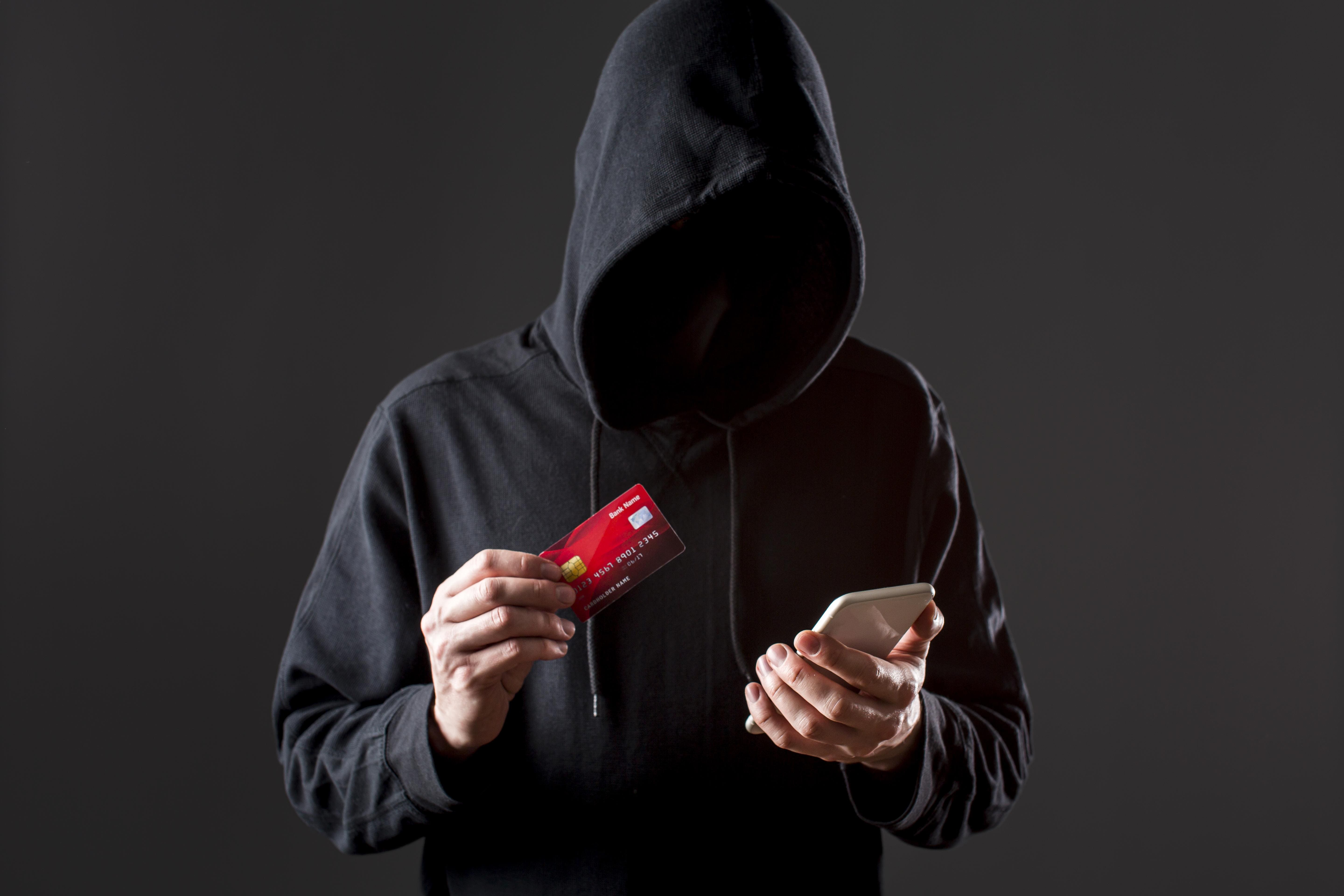 front-view-male-hacker-holding-smartphone-credit-card (1)